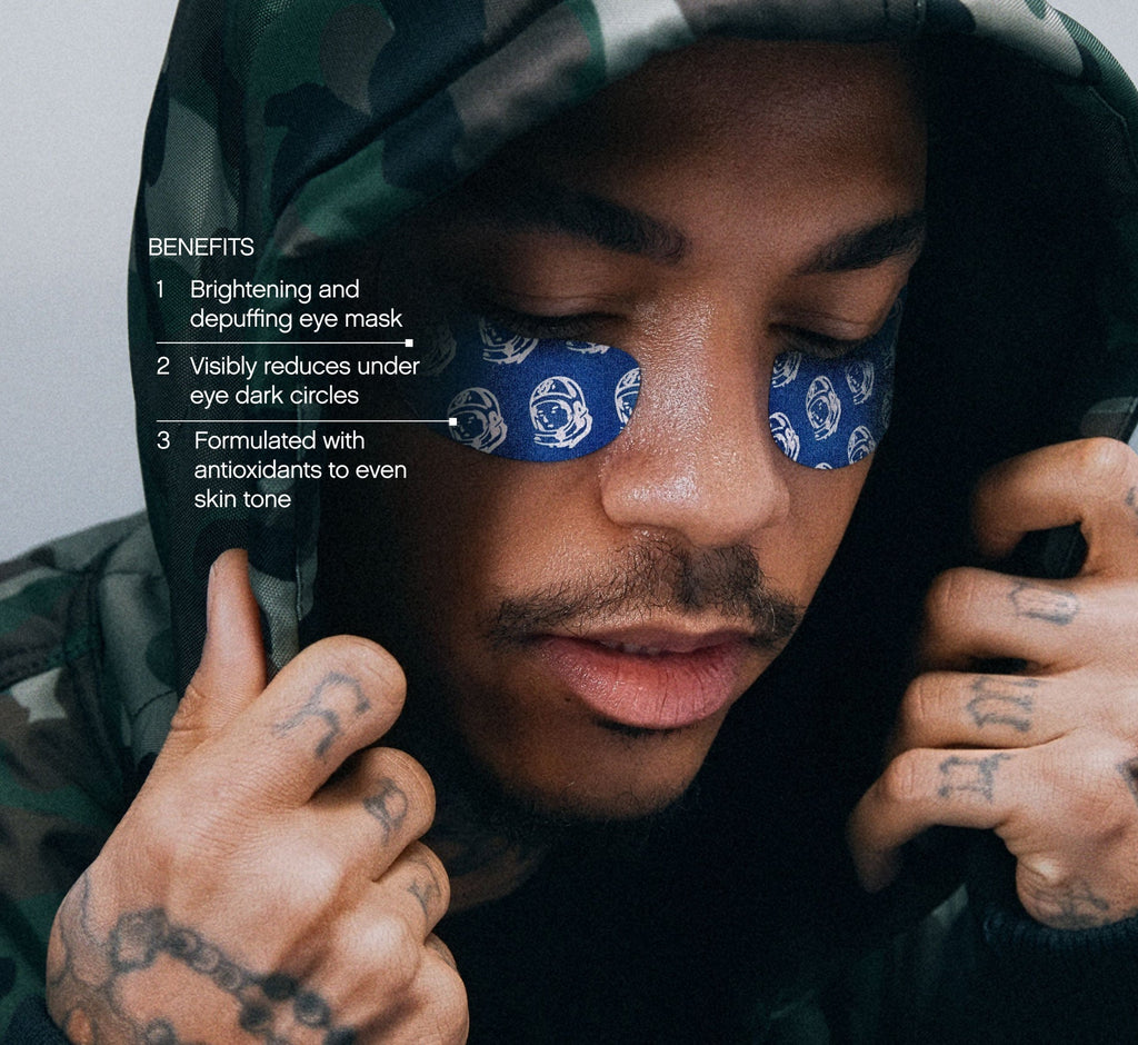 Eye patches for puffiness from Topicals shown applied across both eyes of a tattooed man in a camo hoodie, with benefits callouts for dark circle reduction and skin tone evening.